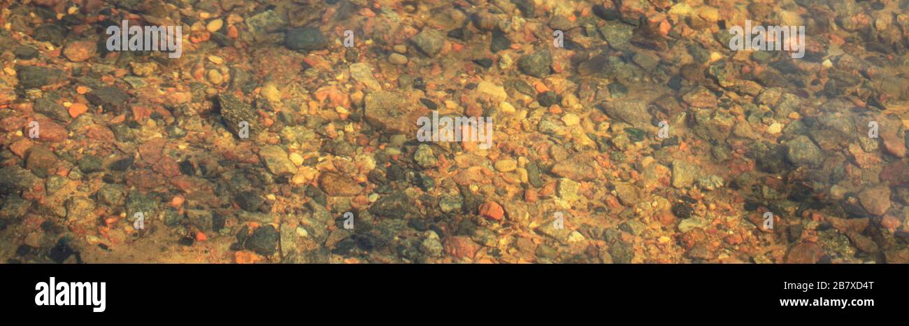 The texture of the river bottom with granite pebbles through the clear spring water. Abstract paints and sketches of nature. Surrealistic palette Stock Photo