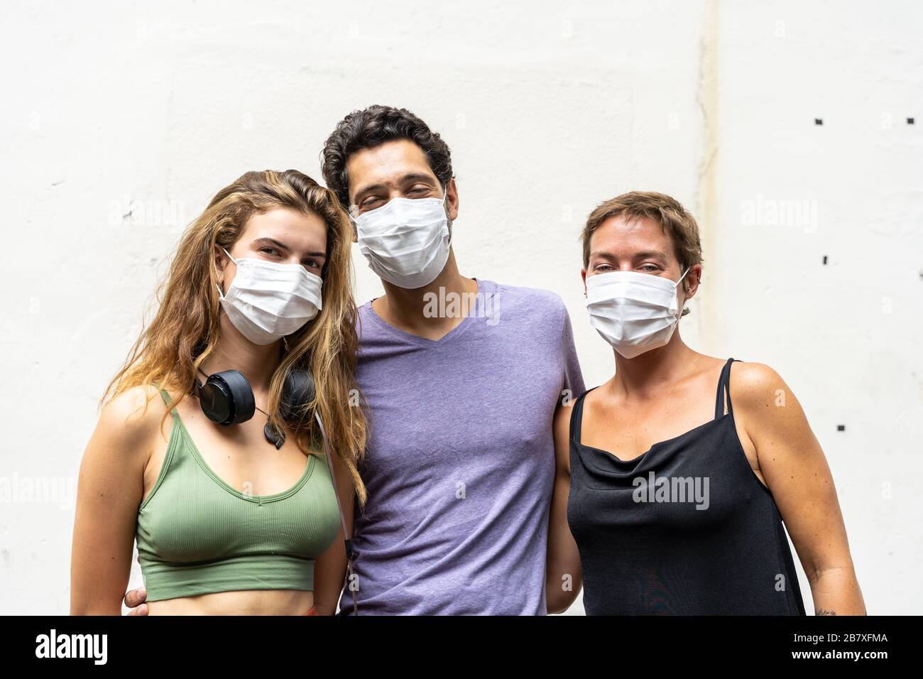 three caucasian people with a mask on their face next to a wall Stock Photo