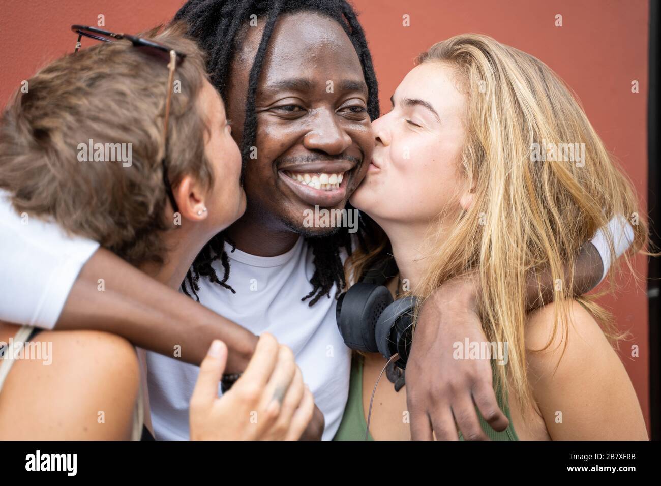 Two blonde girls kissing an African boy by a wall. Multicultural group Stock Photo