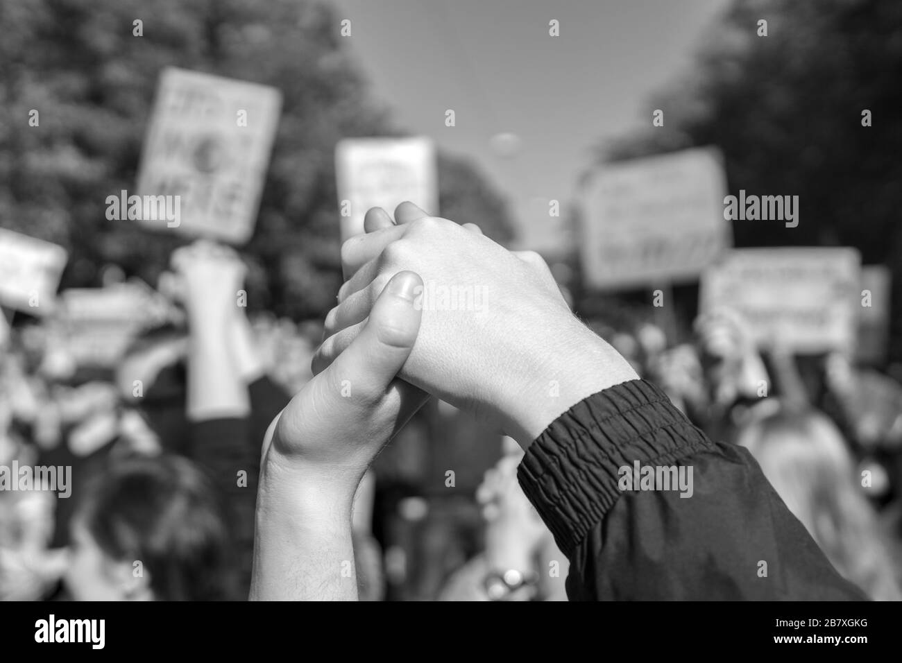 photograph in black and white of two people joining hands together at a fridays for future protest regarding climate change, symbolizing strength Stock Photo