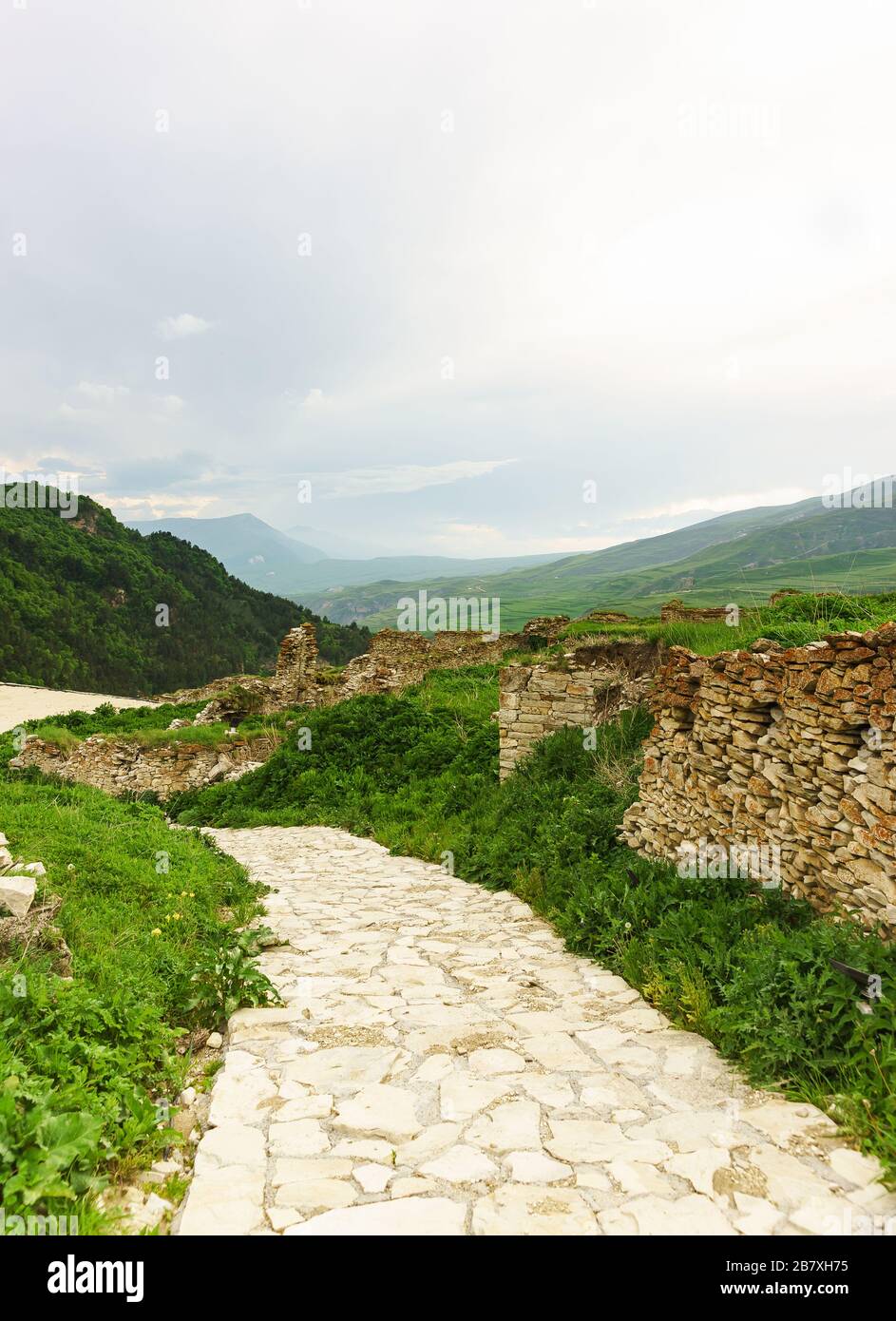 Stone path in the ancient settlement of Hoi against the backdrop of the picturesque mountains of the Greater Caucasus. Masonry without mortar. Cloudy Stock Photo