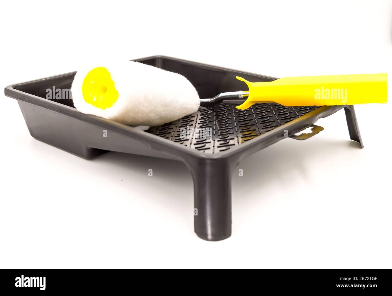 A clean paint roller rests on a black paint tray. Isolated on white