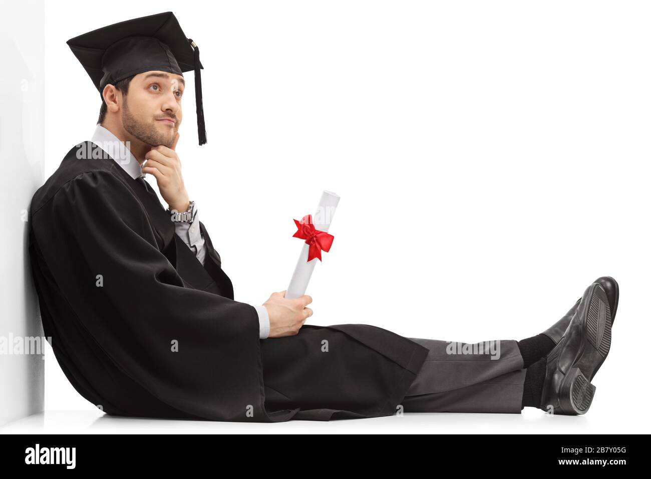 Pensive graduate male student holding a diploma sitting on the floor ...