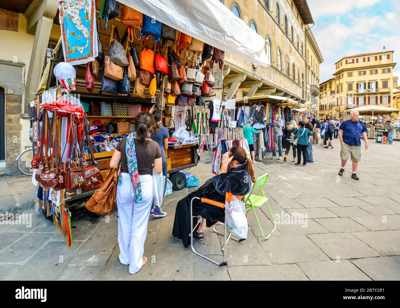 A female tourist buys souvenirs from a small shop stand selling leather goods and clothing in Piazza Santa Croce in Florence Italy Stock Photo