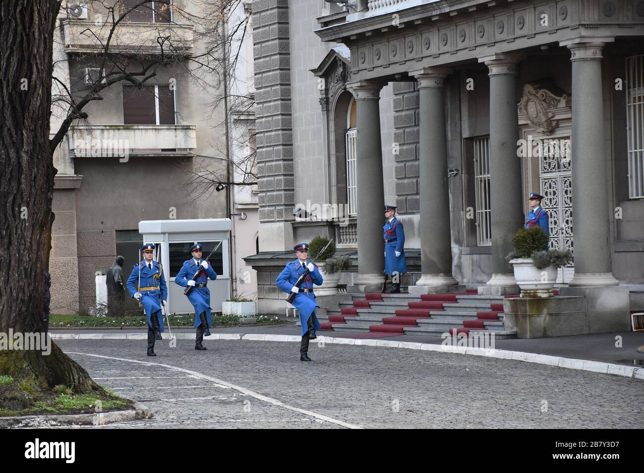 Soldiers in ceremonial blue uniforms with rifles are marching in front of the Serbian presidency building Stock Photo