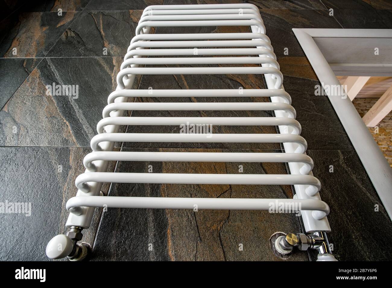 White contemporary electric towel dryer mounted on black tiled wall in