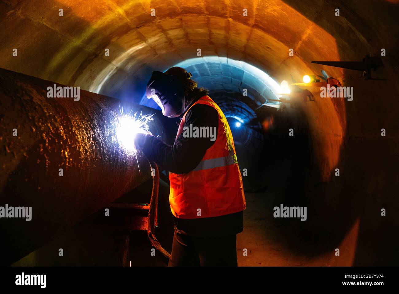 Worker in protective mask welding pipe in tunnel Stock Photo