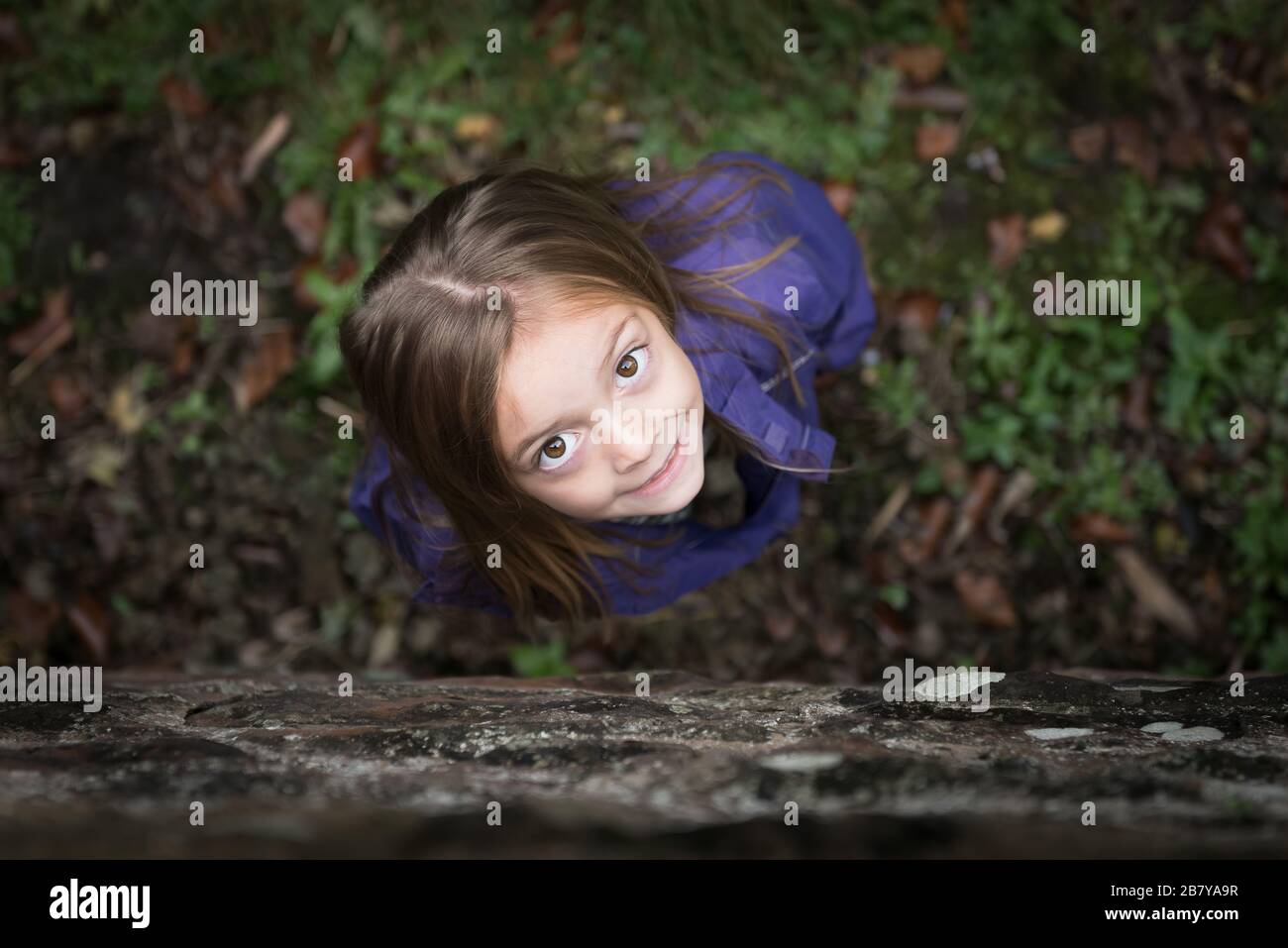 A young girl with large brown eyes looks up at the camera, the image focuses on her eyes and has a narrow depth of field Stock Photo