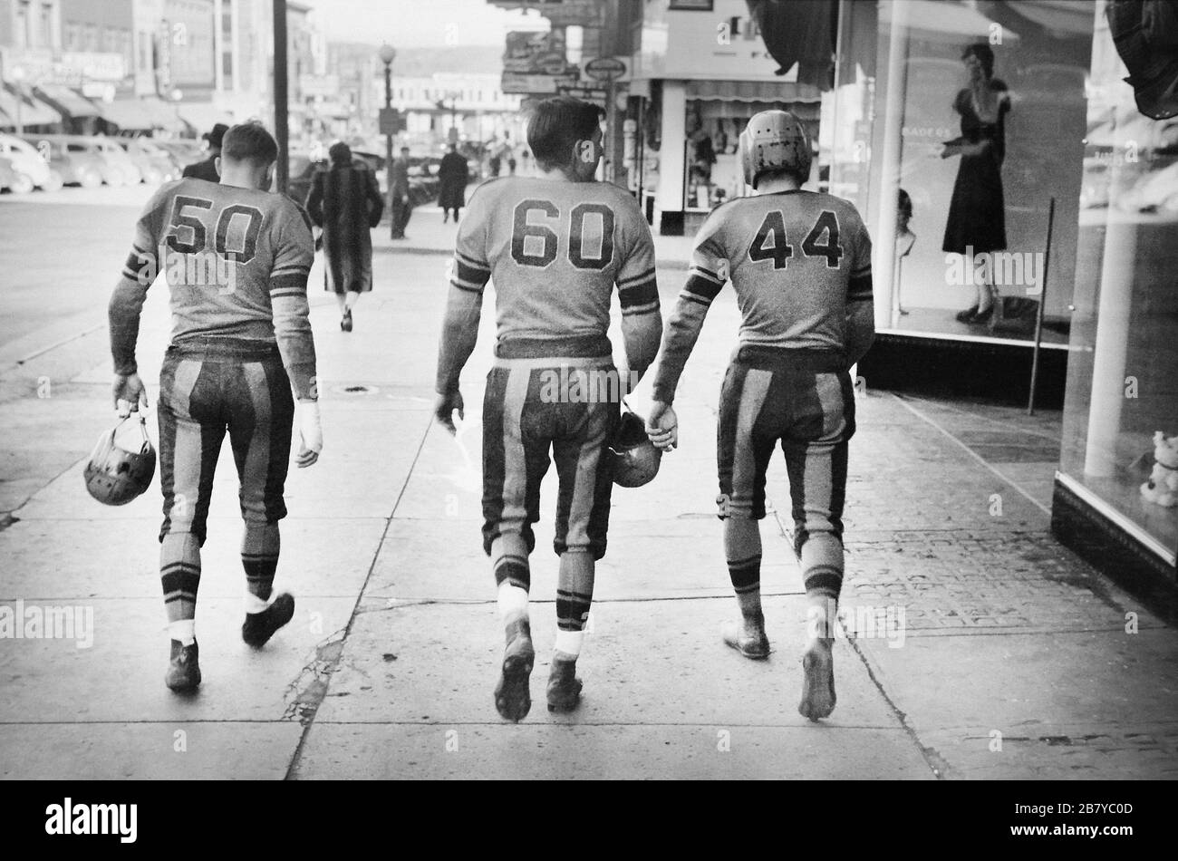 Rear View of Three High School Football Players in Uniforms walking down Street, Minot, North Dakota, USA, John Vachon for U.S. Farm Security Administration, October 1940 Stock Photo