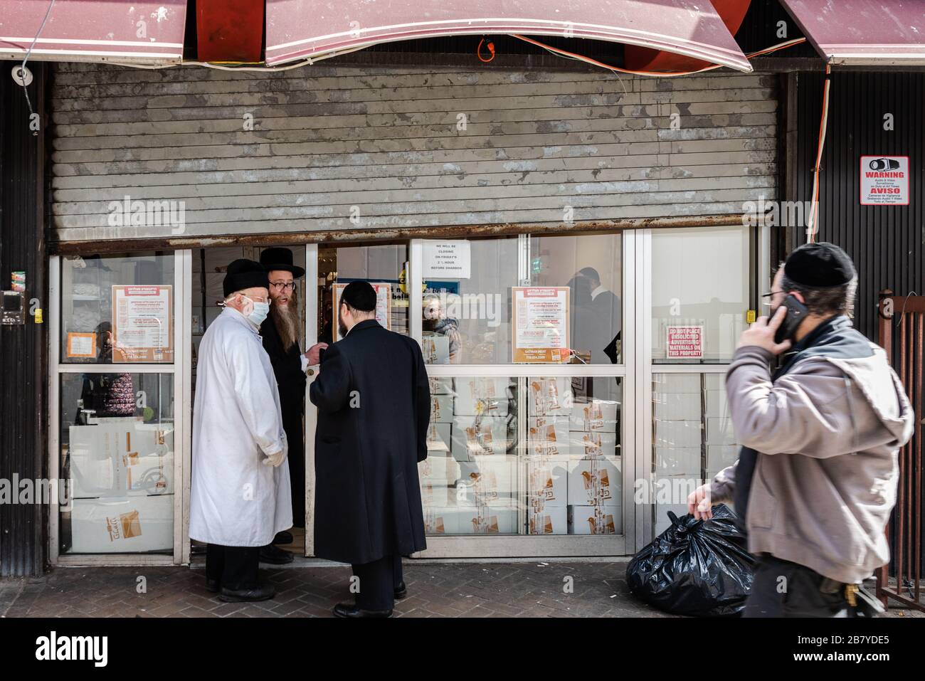 Brooklyn, USA . 18th Mar, 2020. Members of the Hasidic community stand outside a meat market in the Borough Park neighborhood of Brooklyn on March 18, 2020. At least 100 people have tested positive for Coronavirus in the predominantly Hasidic community since Friday. (Photo by Gabriele Holtermann-Gorden/Sipa USA) Credit: Sipa USA/Alamy Live News Stock Photo