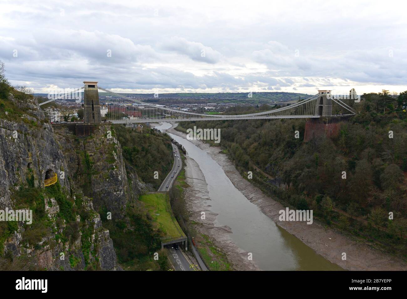 Brunel's Clifton Suspension Bridge on a cloudy day at low tide, Clifton, Bristol, UK, with the gallery rock shelter over the Portway road below Stock Photo