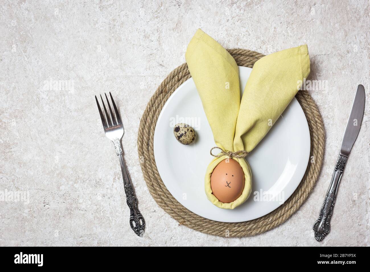 Easter table setting with egg in napkin like Easter Bunny and cutlery. Holidays background, top view. Stock Photo