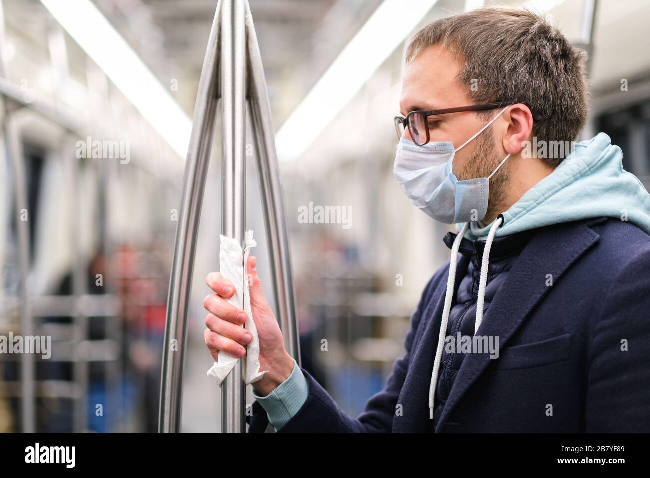 Close up of man holds a handrail in public transport/subway through a napkin, to protect yourself from contact with viruses, germs during a coronaviru Stock Photo