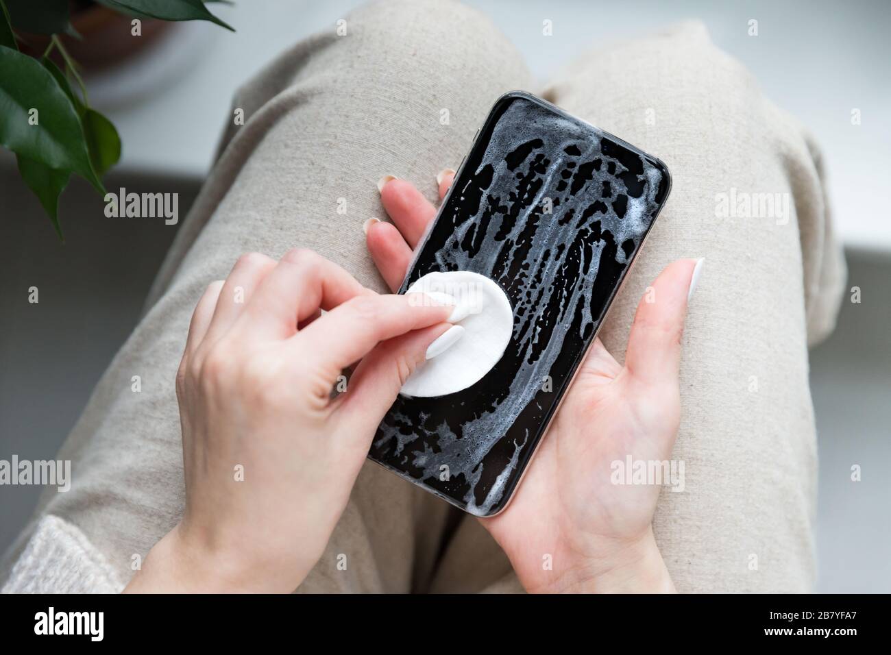 Woman cleaning mobile phone to eliminate germs, coronavirus, covid-19, bacterias. Female disinfects smartphone by applying sanitizer/alcohol disinfect Stock Photo