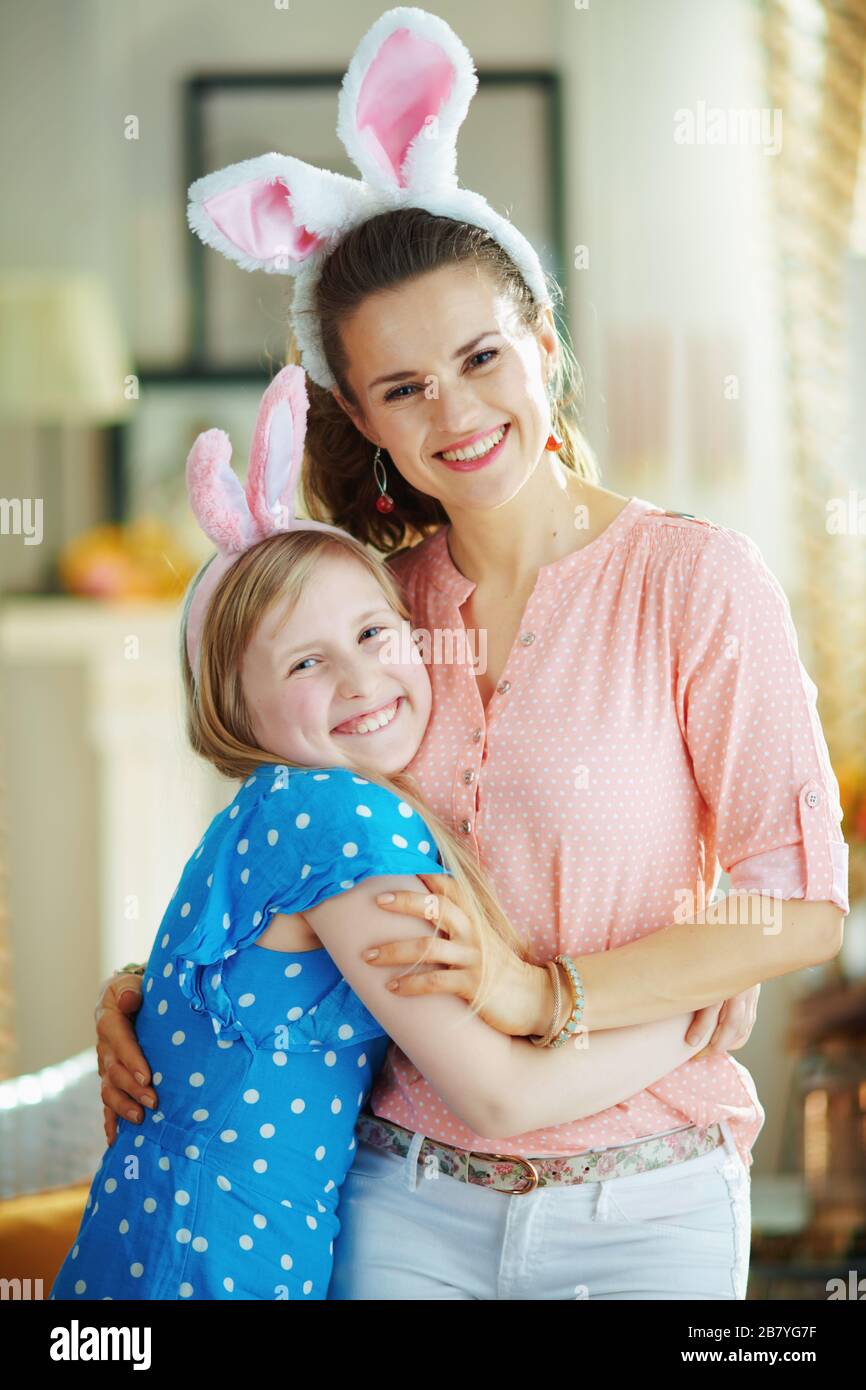 Portrait of happy modern mother and child in easter bunny ears at modern home in sunny spring day hugging. Stock Photo
