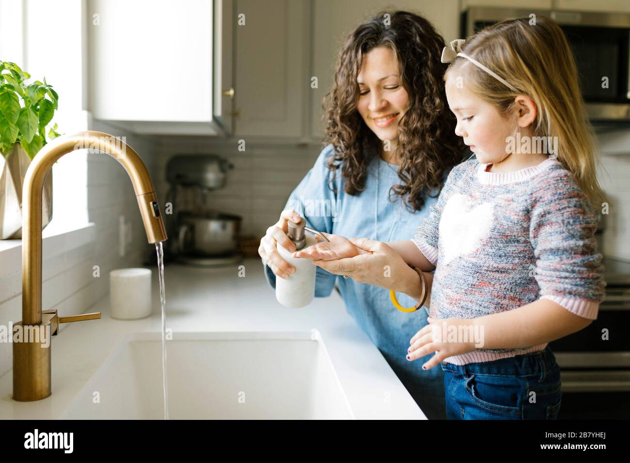 Mother and daughter washing hands in kitchen sink Stock Photo
