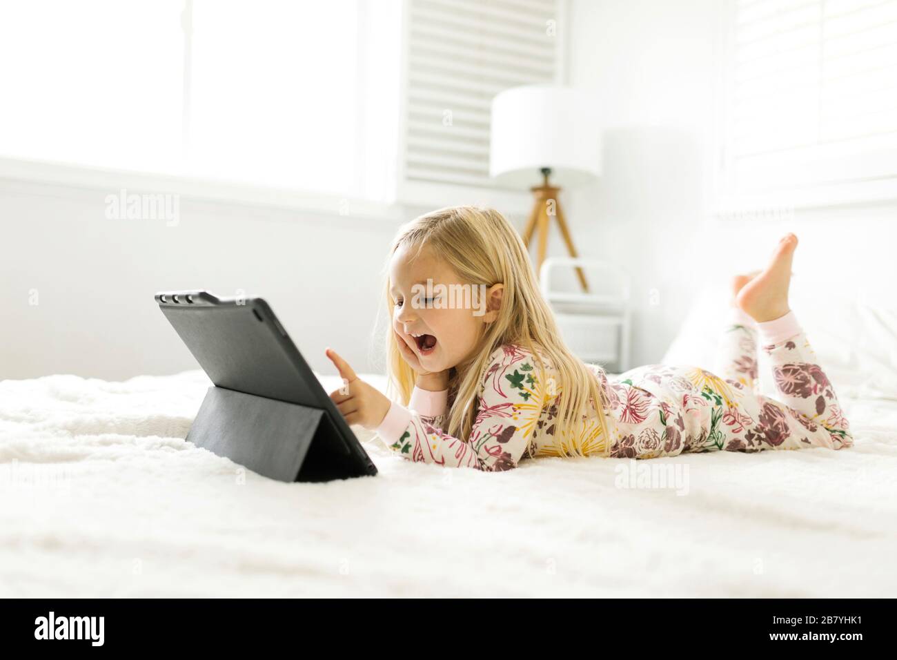 Girl in pajamas using digital tablet while lying on bed Stock Photo