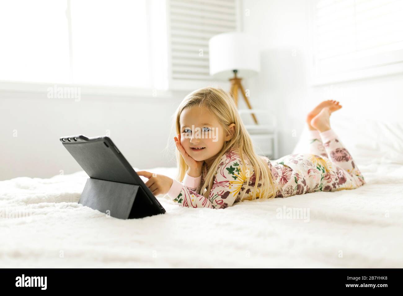 Girl in pajamas using digital tablet while lying on bed Stock Photo