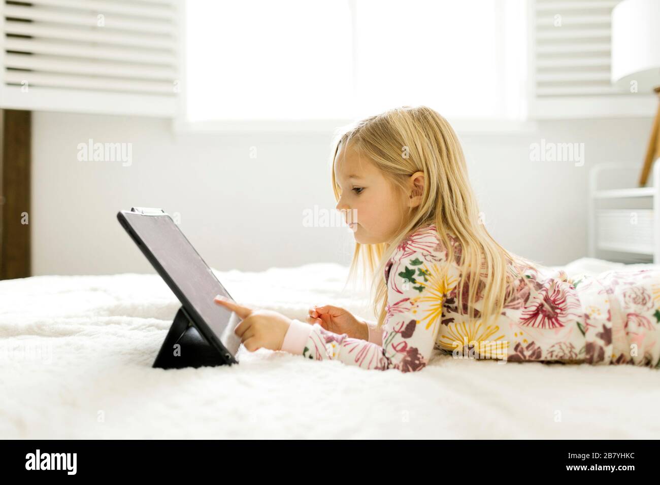 Girl in pajamas using digital tablet while lying on bed Stock Photo