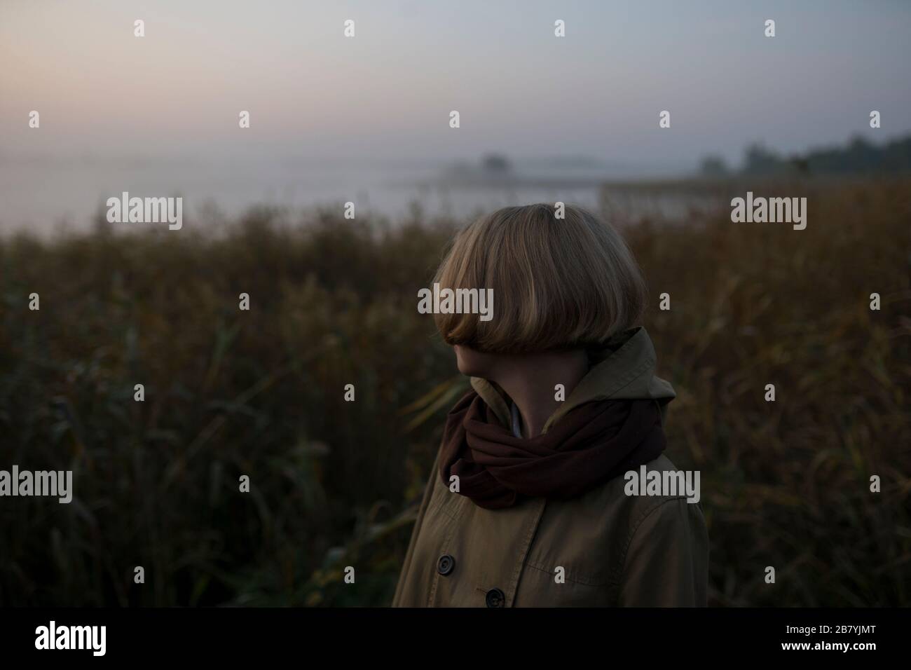 Young woman in field by lake at sunset Stock Photo