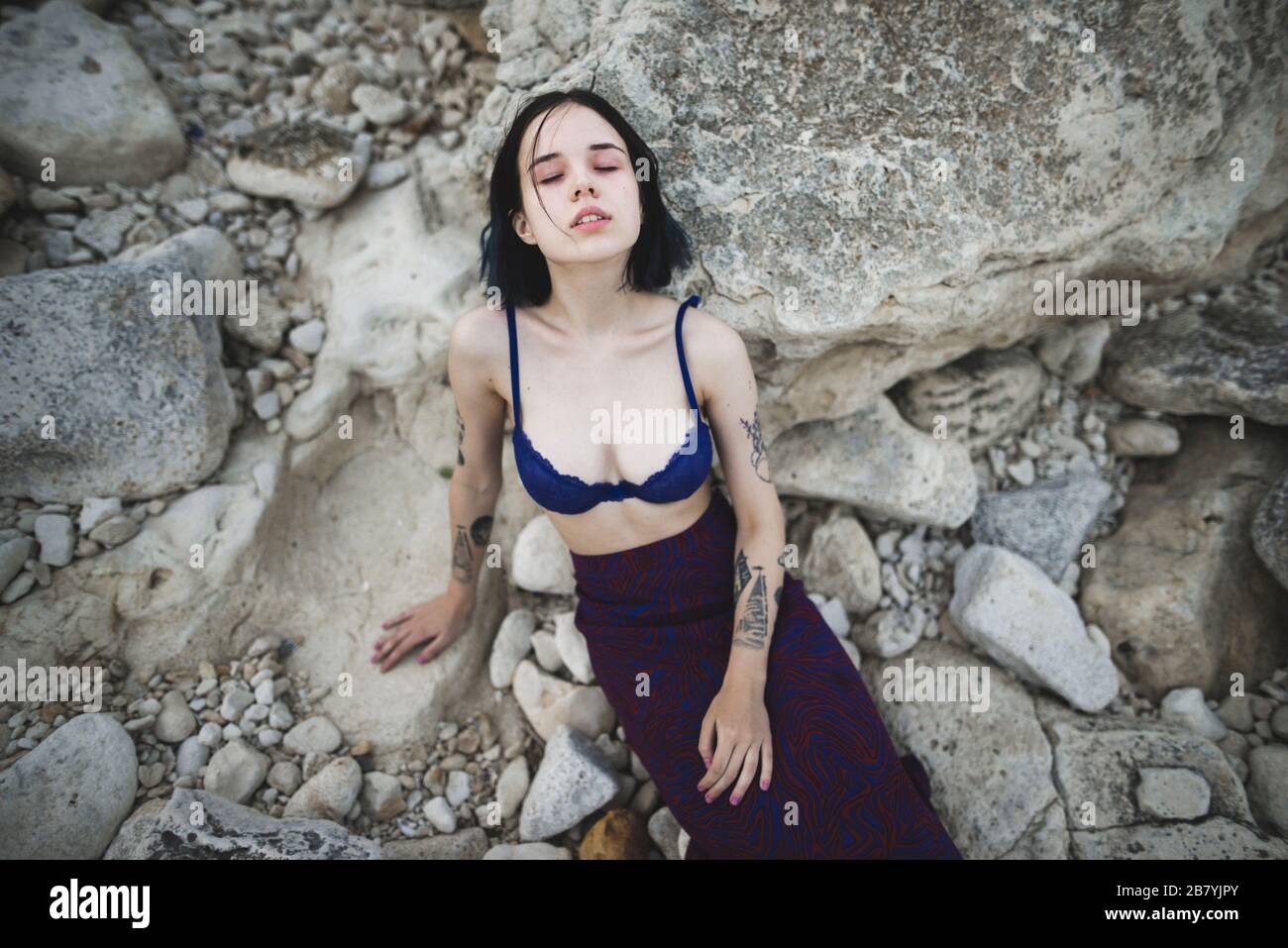 Tattooed woman in blue bra sitting on rocks Stock Photo