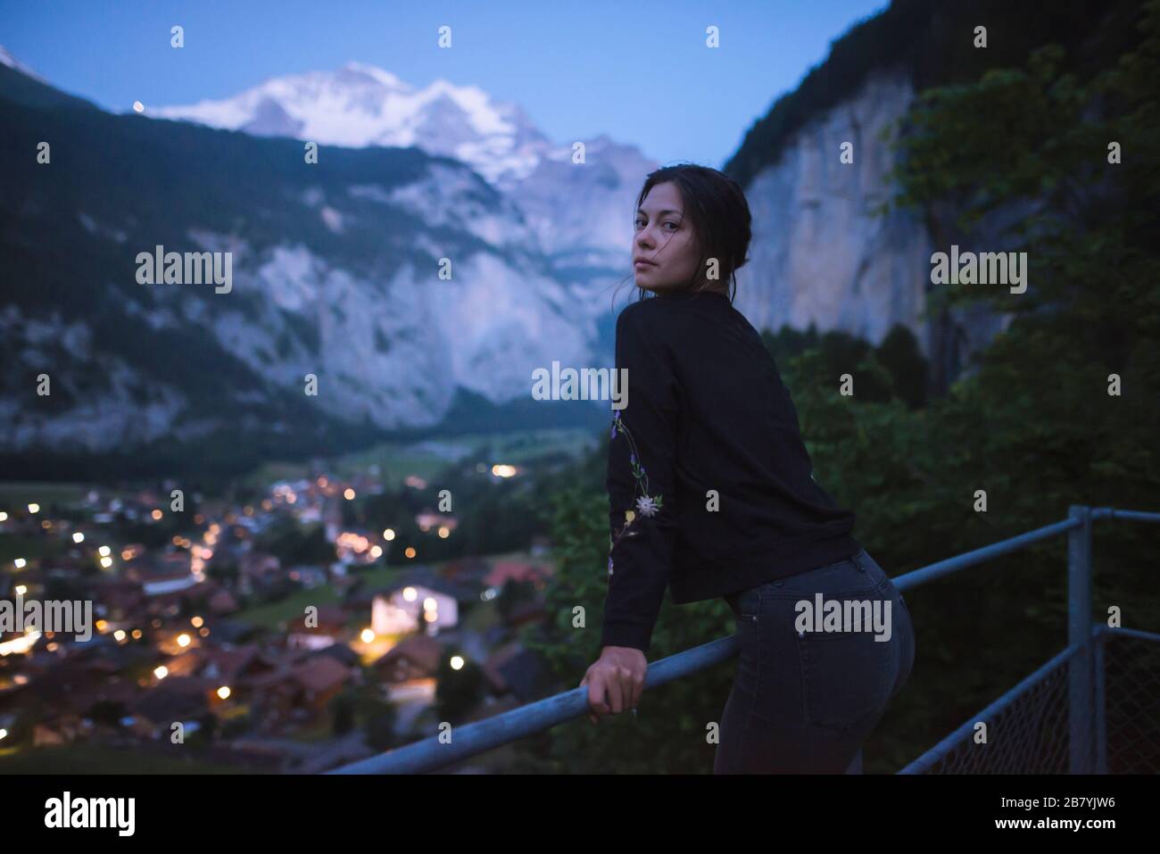 Young woman leaning on railing by mountain and village Stock Photo