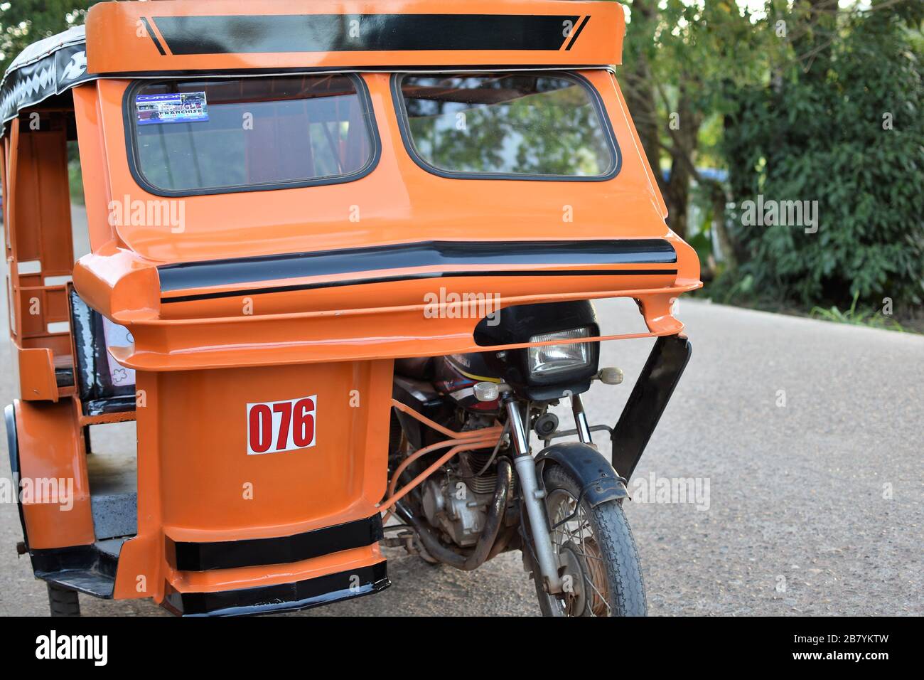An orange tricycle is parked on the side of the road in Coron, Palawan in the Philippines Stock Photo