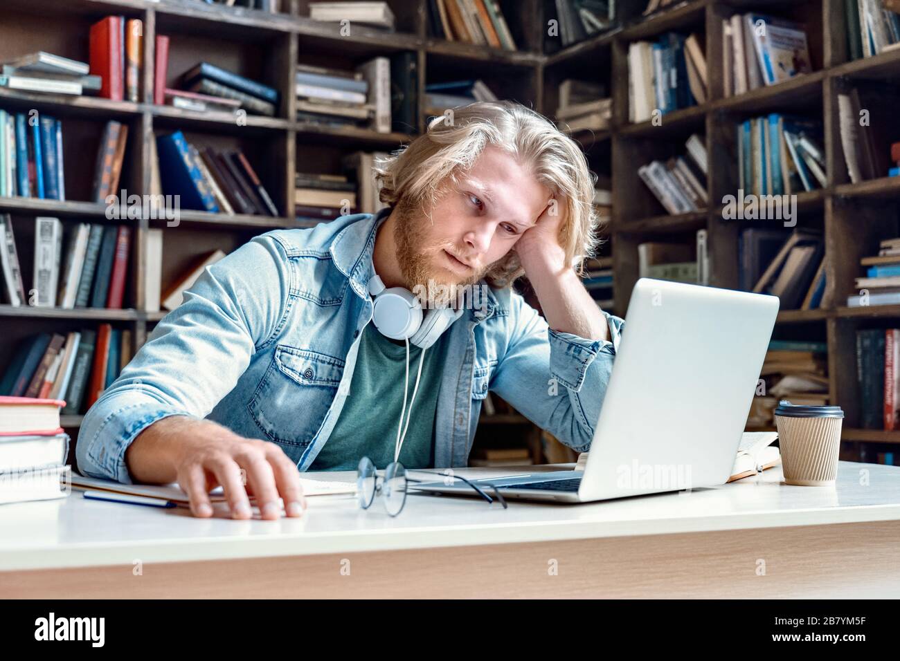 Unhappy bored male student studying looking at laptop. Stock Photo