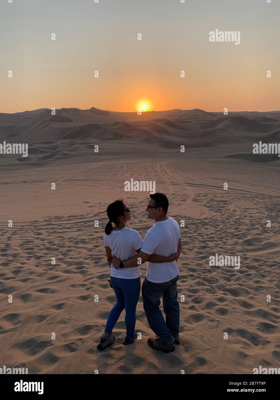 Couple enjoying the view of beautiful sunset at Huacachina Oasis in Peru Stock Photo