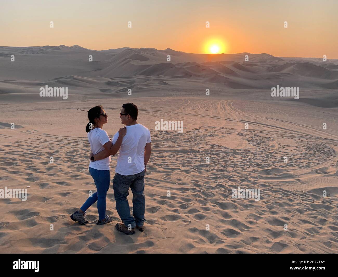 Couple enjoying the view of beautiful sunset at Huacachina Oasis in Peru Stock Photo