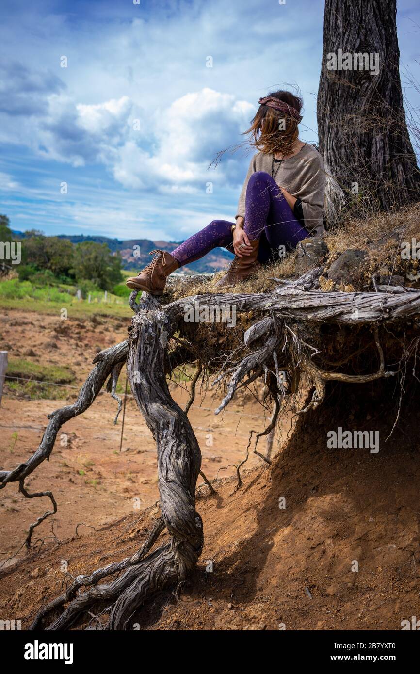 hippie girl connecting with nature sitting on a tree with roots out of the ground in mexico Stock Photo