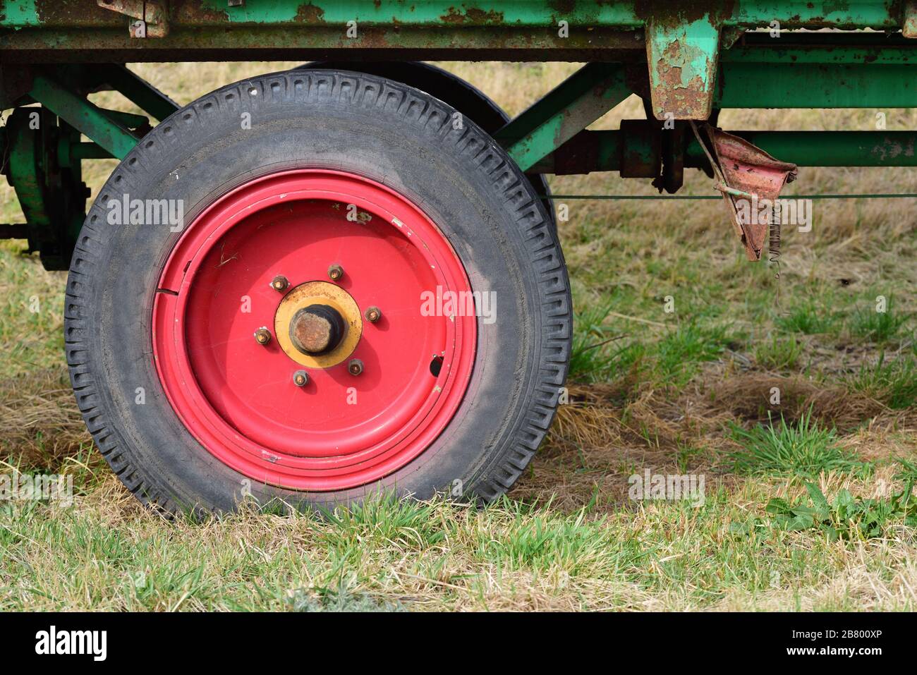 Detail of an old agricultural vehicle, with a red old wheel and tires, on a meadow Stock Photo