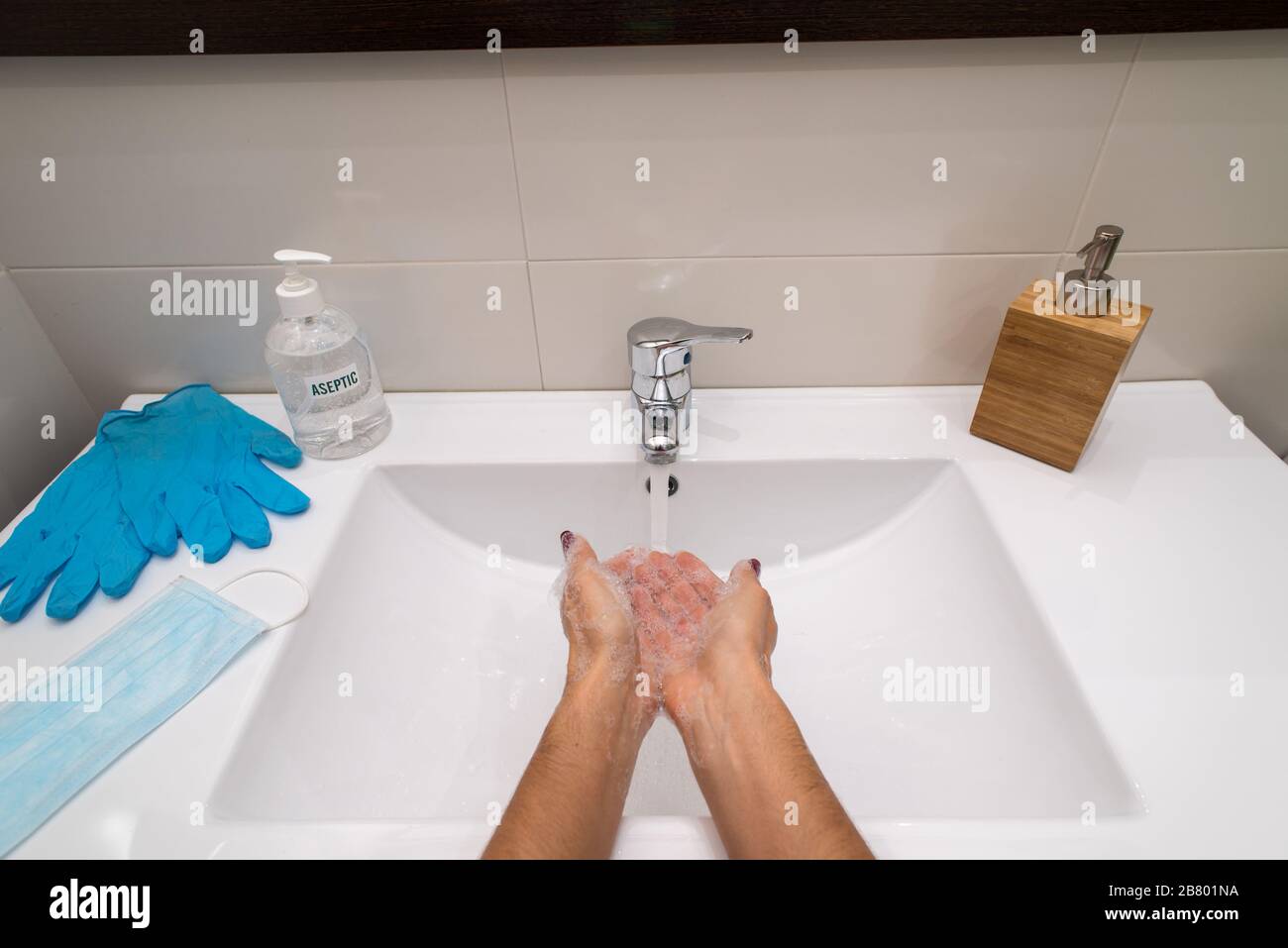 Person washing soapy hands in a sink with material to prevent coronavirus (covid-19), hydroalcoholic gel, soap, gloves and mask. Stock Photo