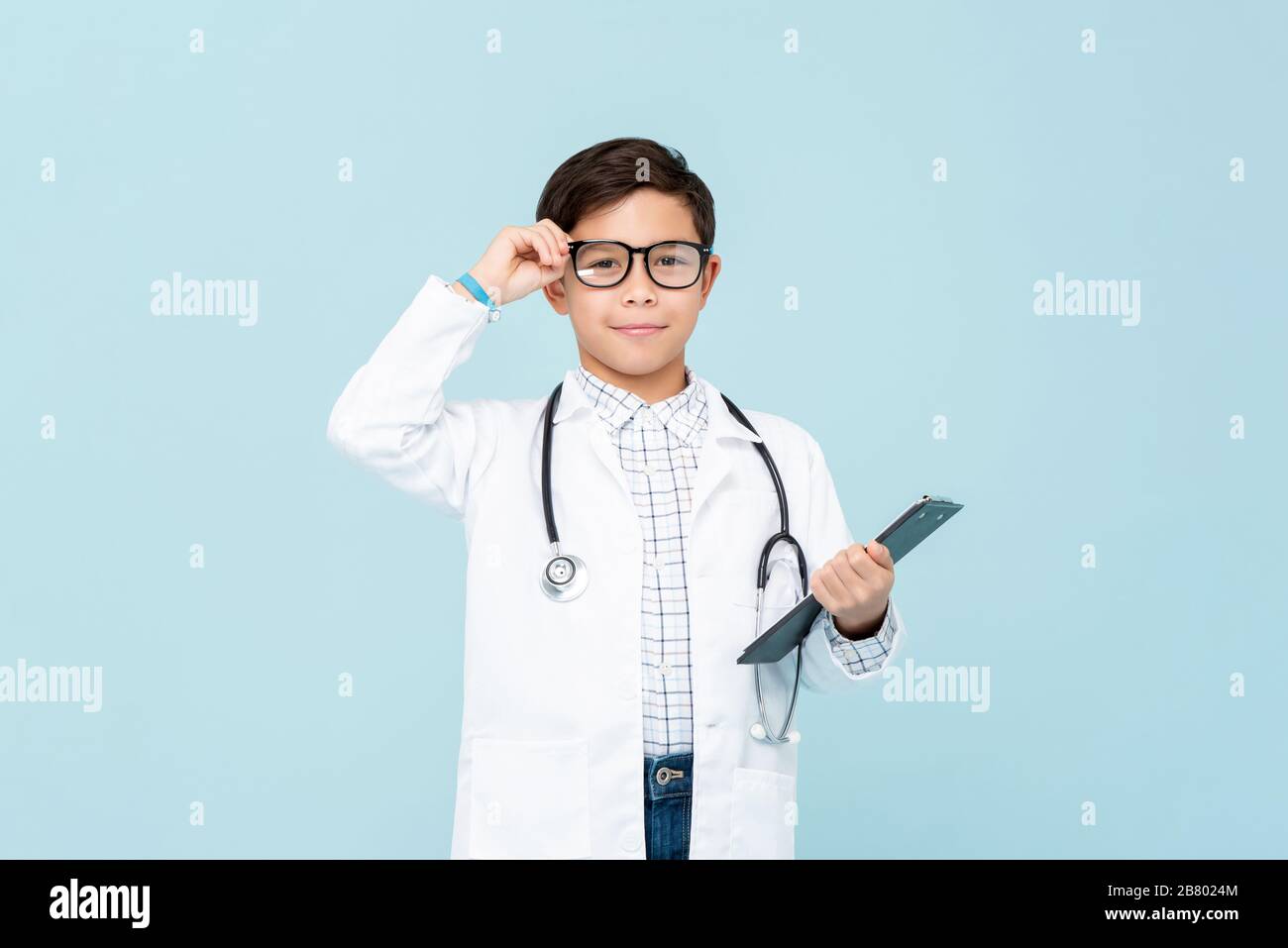 Smiling smart doctor boy with white medical coat and stethoscope isolated on light blue background Stock Photo