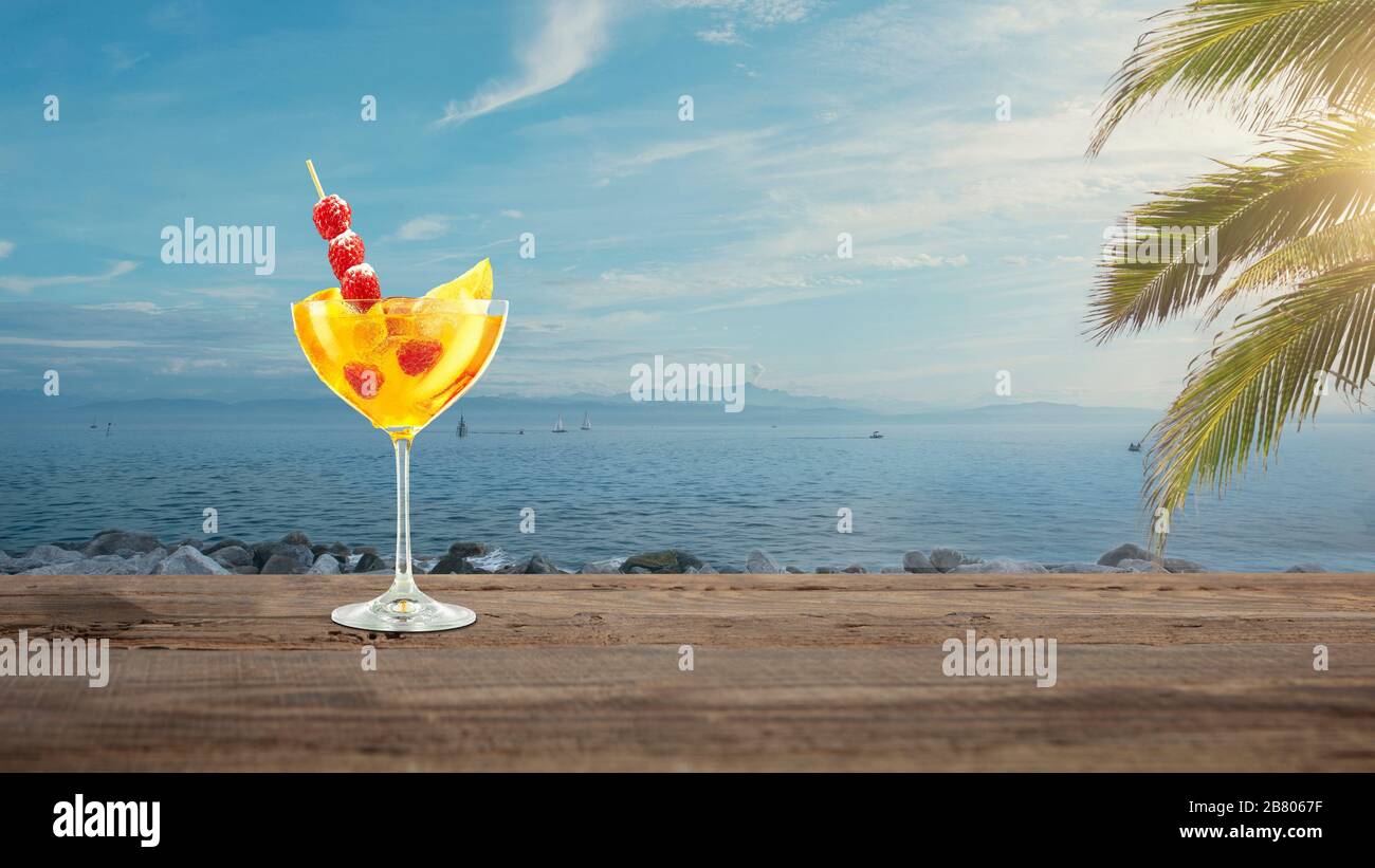 Travel Summer Bright And Tasty Refreshing Cocktail With Sea Or Ocean Beach With Palms And White Sand On Background Yellow Alcohol Drink With Berries Concept Of Summertime Vacation Resort Chill Stock Photo