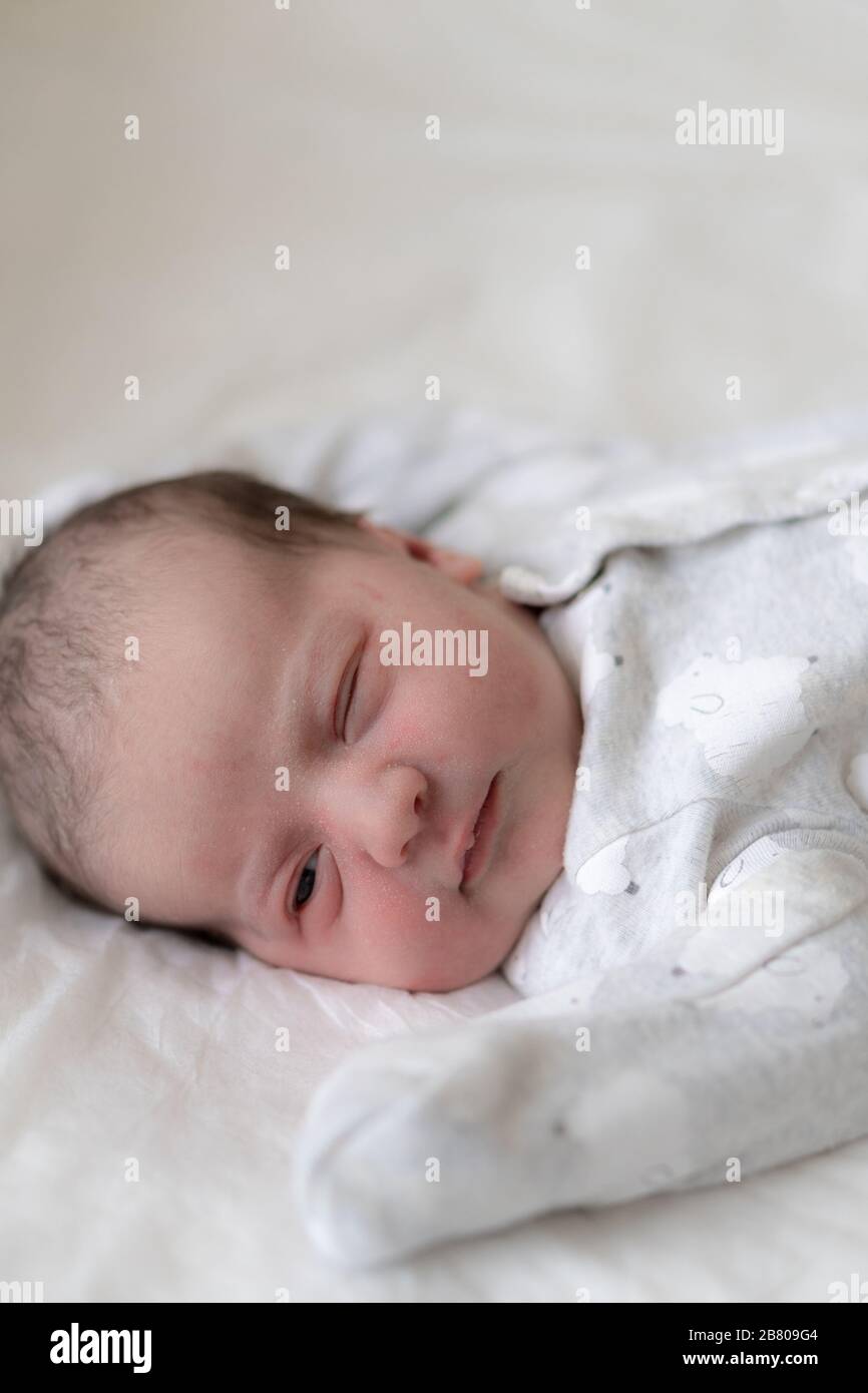 A newborn baby lies on its back and opens one eye in the first minutes