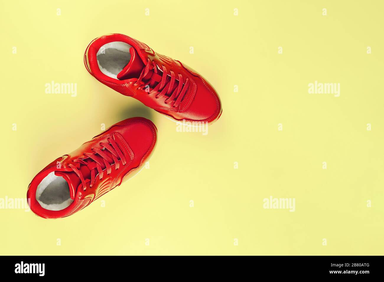 Red sneakers on pastel yellow background. Concept of sport and healthy lifestyle. Place for text, flat lay, top view, vertical. Stock Photo