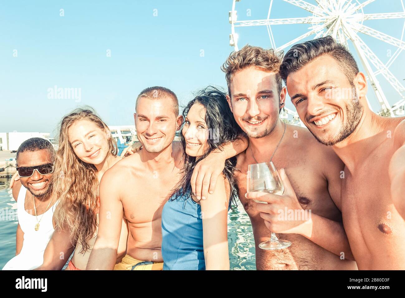Group of multiracial friends having fun in boat summer party - Young people taking selfie photo with ferris wheel in background - Happiness and friend Stock Photo