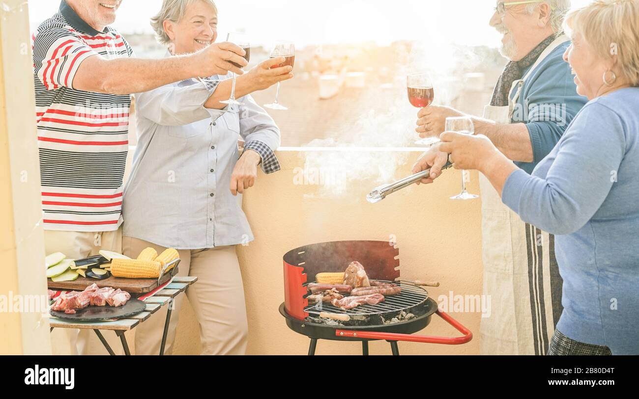 Happy senior friends having fun at barbecue meal in terrace outdoor - Mature old people dining and drinking wine at bbq lunch - Focus on left hands fa Stock Photo