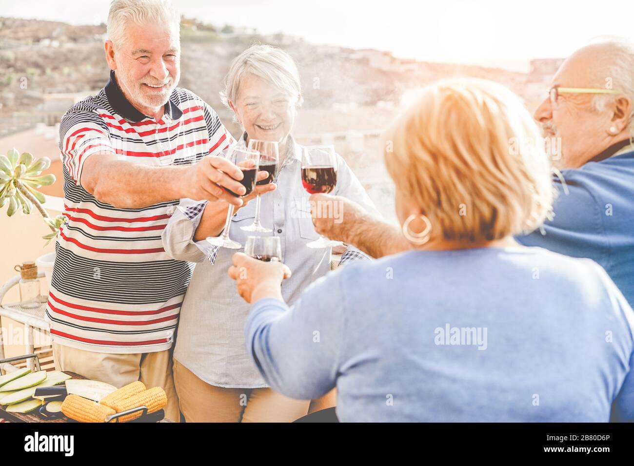 Group of happy senior friends cheering at barbecue meal in patio terrace outdoor - Mature old people dining and drinking wine at bbq lunch - Focus on Stock Photo