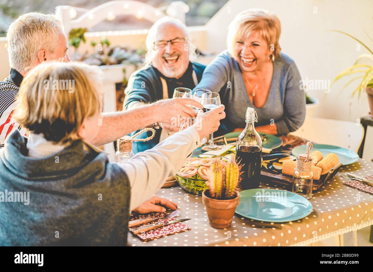 Group of happy senior friends cheering at barbecue meal in terrace outdoor - Mature old people drinking wine at patio bbq dinner - Main focus on left Stock Photo