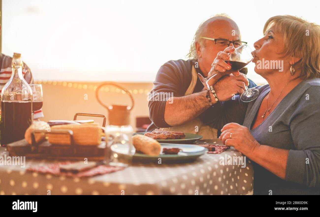Senior couple having fun at dinner in home patio - Pensioner enjoying summer vacation eating and drinking wine - Focus on hands glasses - Love, relati Stock Photo