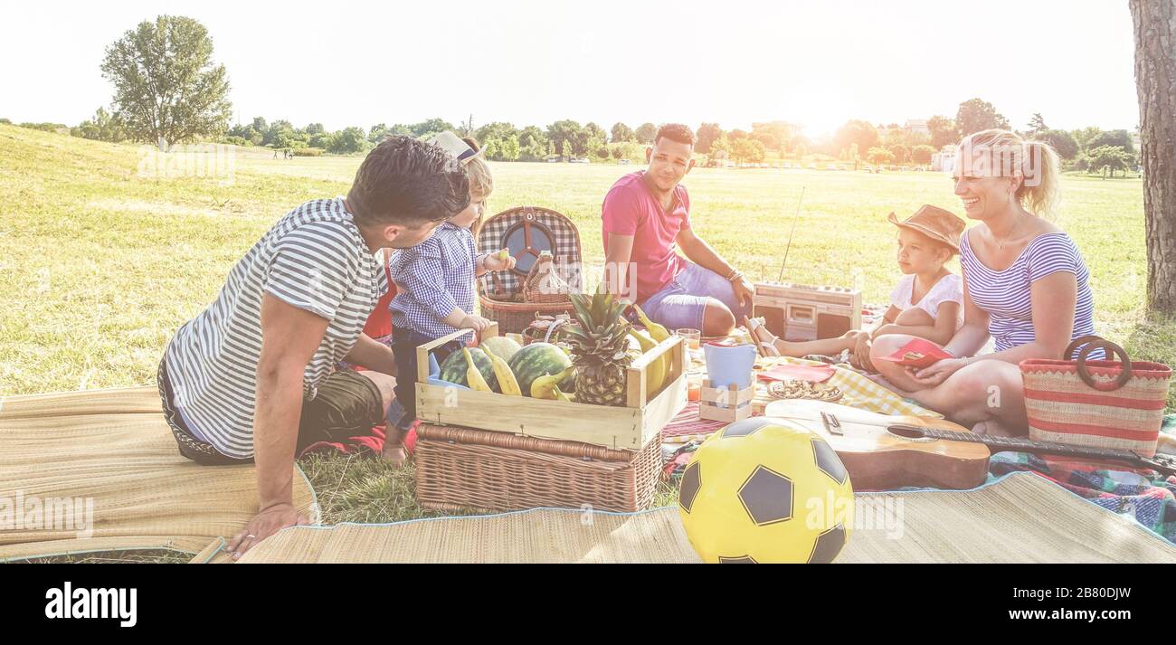 Happy families doing picnic in nature park outdoor - Young parents having fun with children in summer eating fresh fruit and laughing together - Love Stock Photo