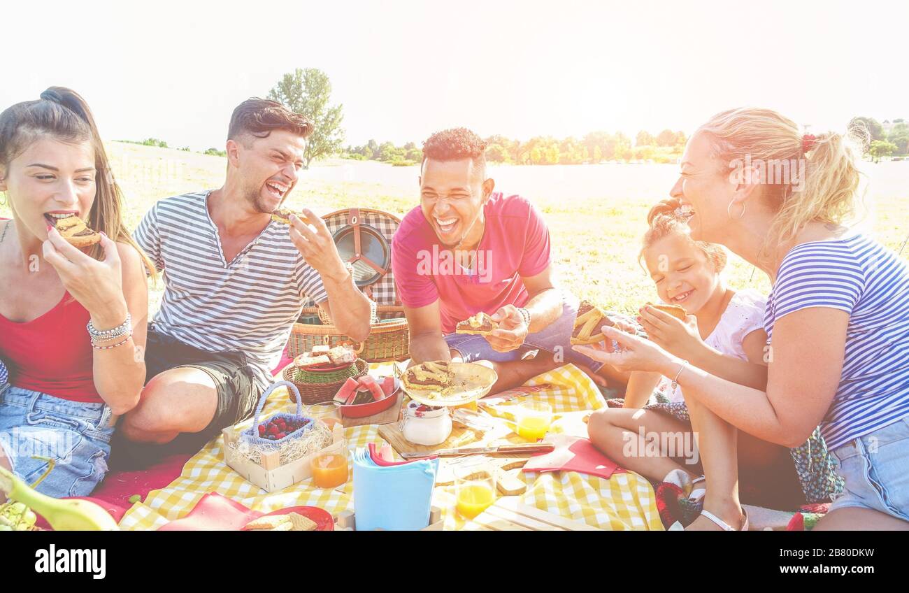 Happy families doing picnic in nature park outdoor - Young parents having fun with children in summer time eating cake and laughing together - Love an Stock Photo