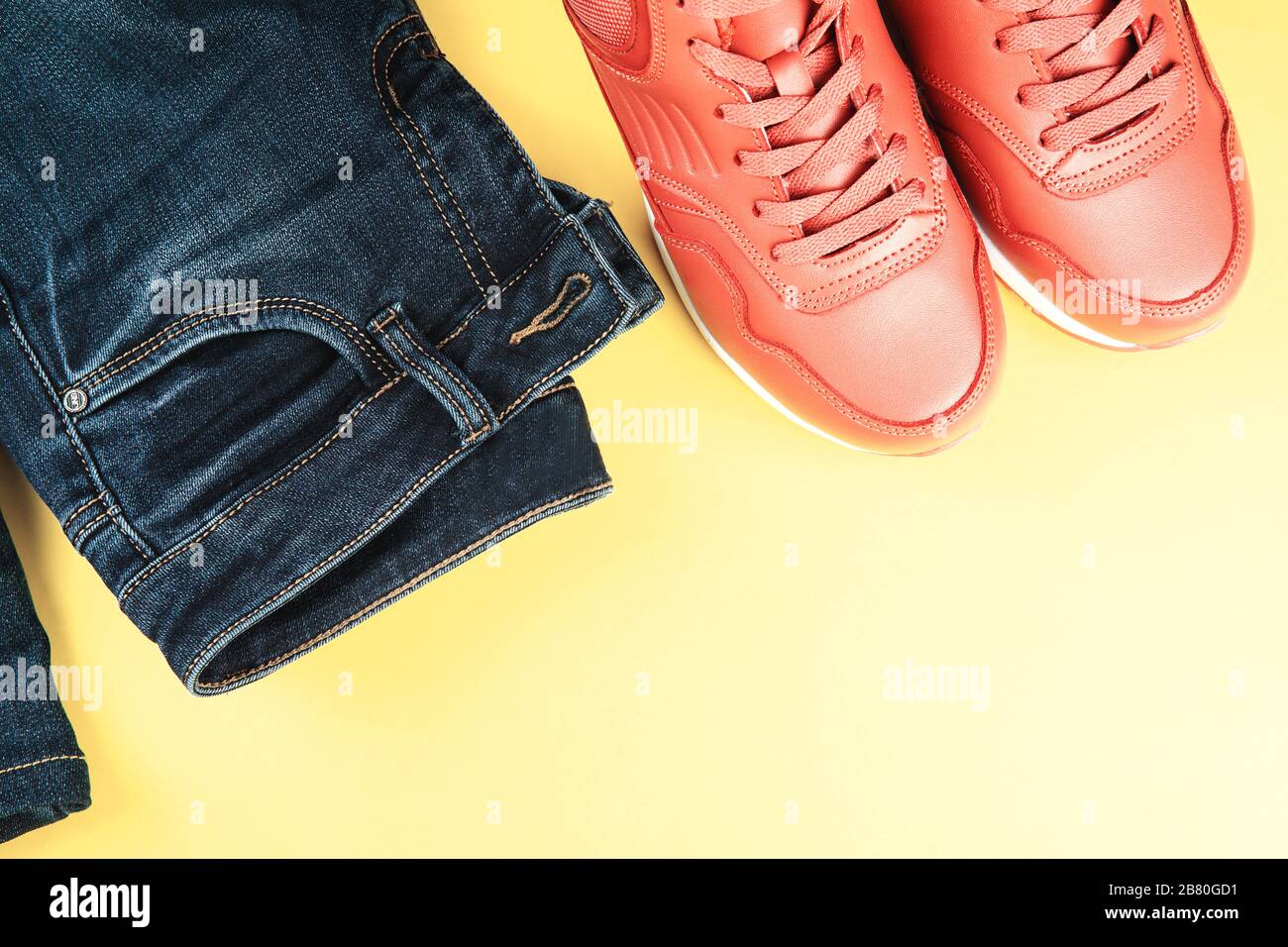 Pink sneakers and blue jeans on pastel yellow background. Concept of sport lifestyle and casual style. Place for text, flat lay, top view. Stock Photo