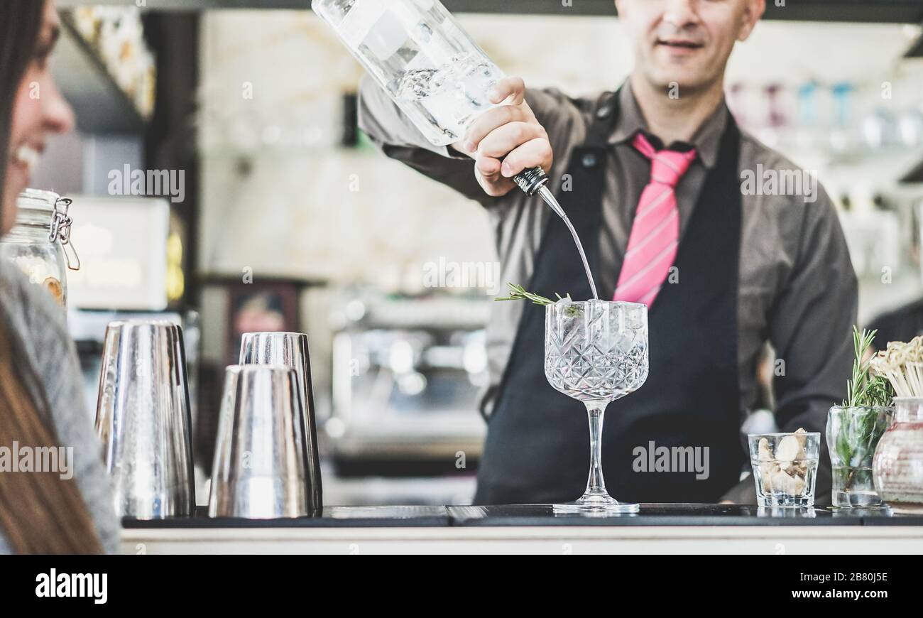Bartender mixing cocktail in a trendy crystal glass with aromatic herbs  - Young people waiting for drink at party disco bar - Focus on glass - Nightl Stock Photo