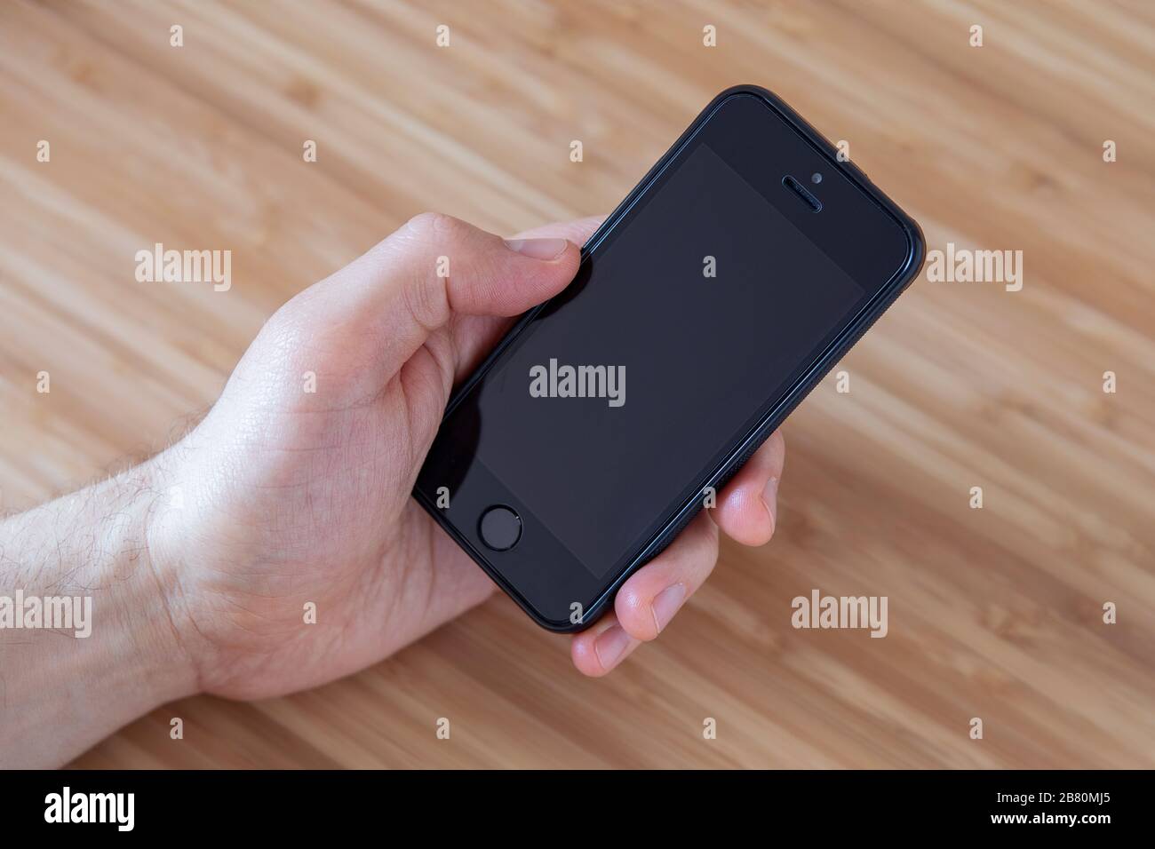 Man holding blank iphone with his left hand, blank display close up, neutral background, view from above. Communication concept. Stock Photo