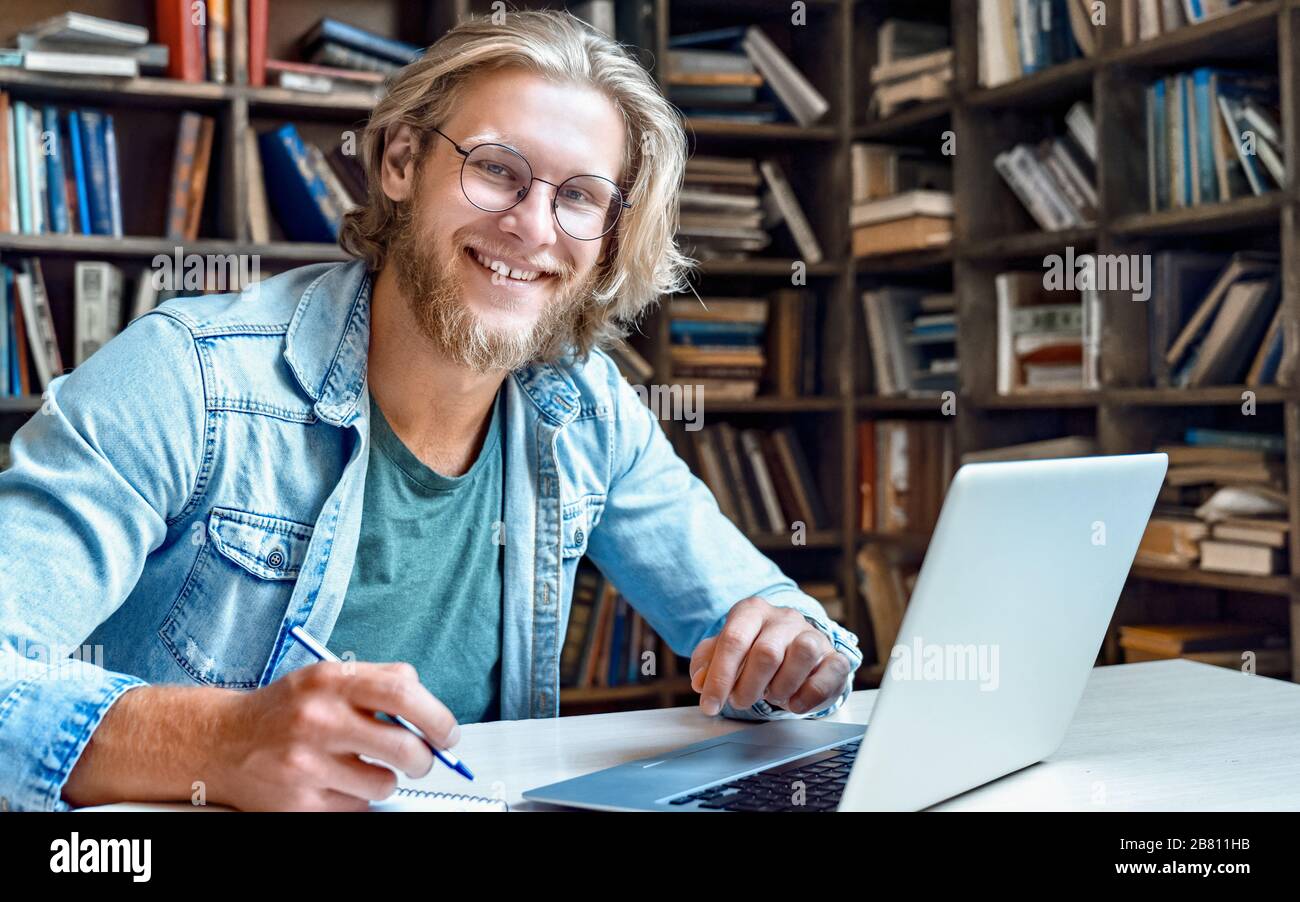 Smiling male student study online on computer make notes in library, portrait. Stock Photo