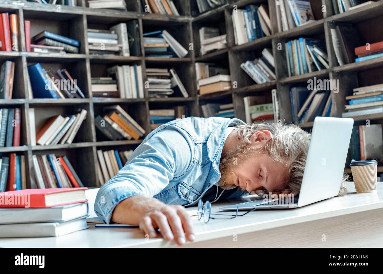 Funny tired sleepy university student sleeping sitting at library desk. Stock Photo