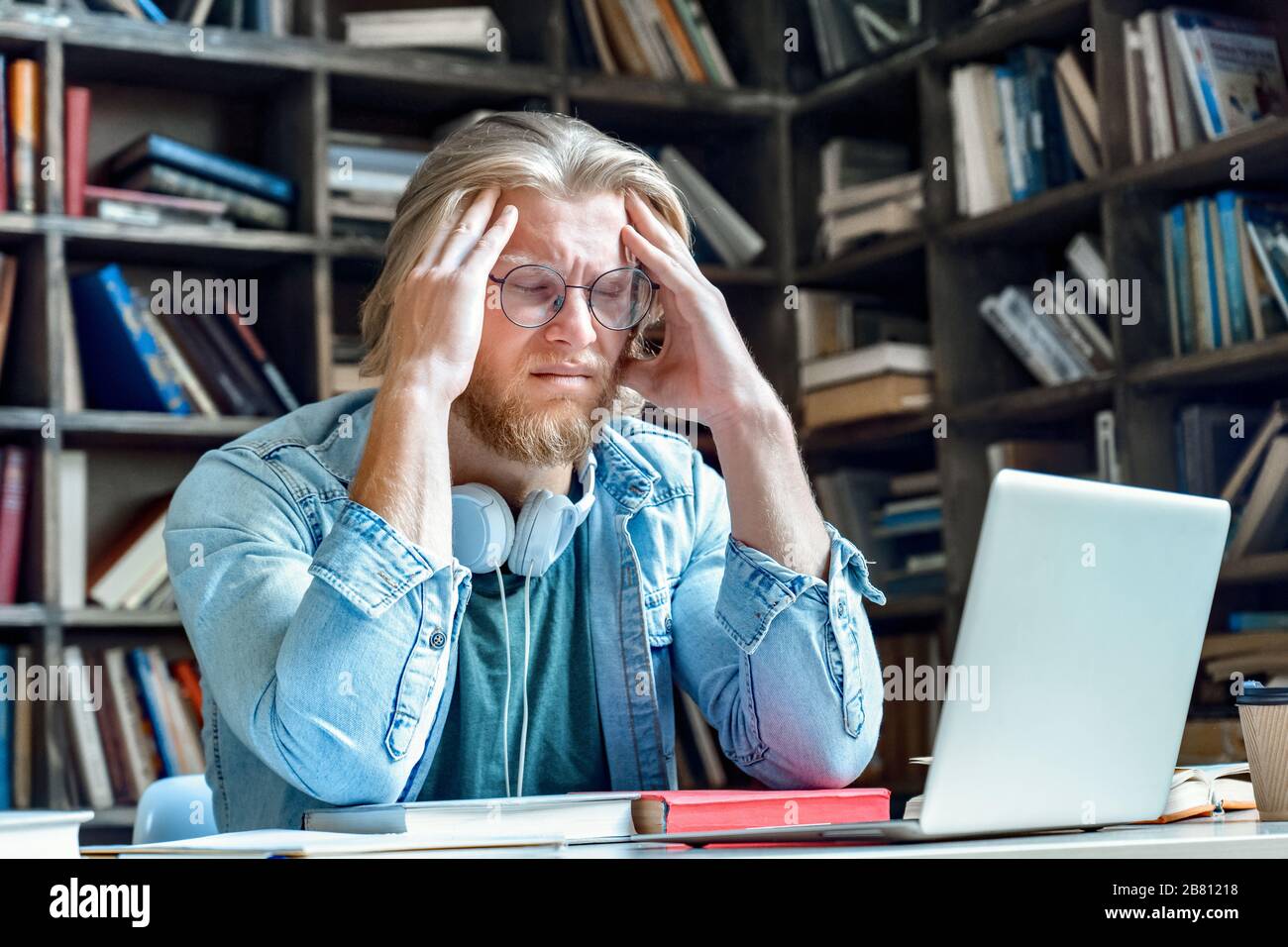 Young stressed tired man in glasses with closed eyes massage head. Stock Photo